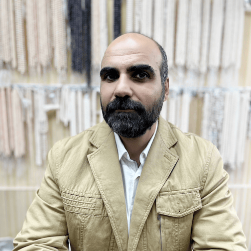 مدیر اجرایی برند مروارید صحرایی در حال پرتره مقابل دیوار آویزهای مهره و مروارید؛ فعال در طراحی و فروش زیورآلات دستساز مانند گردنبند و دستبند