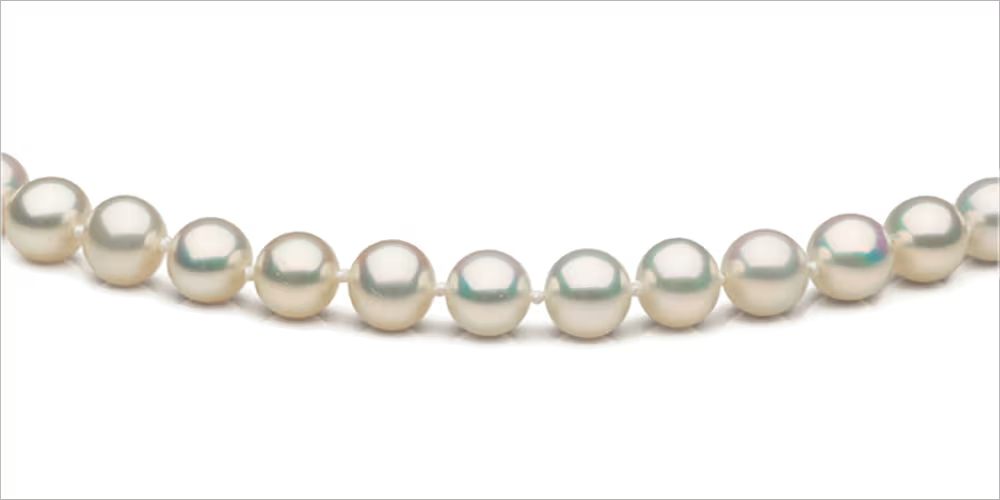 نمای نزدیک از رشتهای مروارید سفید با شکل عمدتاً نزدیک به گرد، درخشندگی خوب تا متوسط و چند نقص سطحی قابل مشاهده؛ نمونهٔ شاخص برای «درجه AA»