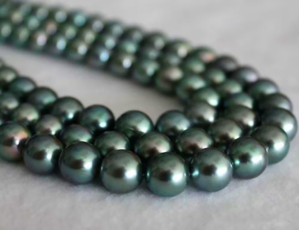 نمای نزدیک از رشتهای از مرواریدهای تاهیتی تیره با شکل عمدتاً گرد و سطح براق؛ نمونهای برای ارزیابی معیار «شکل مروارید»
