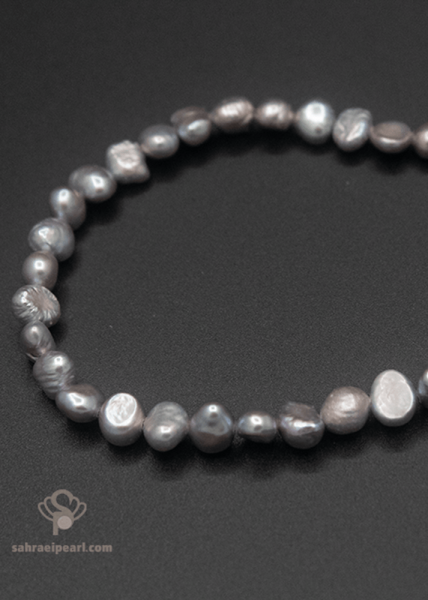 دستبند مروارید باروک طوسی با دانه‌های نامتقارن ۵ تا ۷ میلی‌متری روی پس‌زمینهٔ مشکی